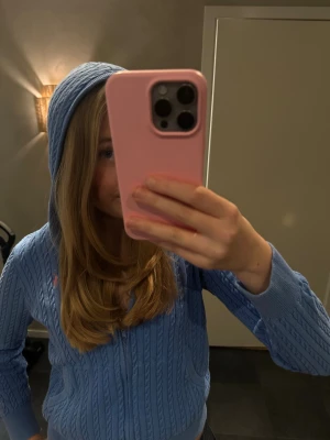 Blå stickad hoodie från Polo Ralph Lauren - Säljer en blå stickad hoodie från Polo Ralph Lauren med dragkedja och huva. Tröjan har ett snyggt kabelstickat mönster, rosa logga på bröstet och praktiska fickor framtill. Croppad passform och långa ärmar gör den både chill och stilren.