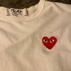 Vit långärmad t-shirt Comme des Garçons - Säljer en clean vit långärmad t-shirt från Comme des Garçons PLAY i storlek S. T-shirten har det ikoniska röda hjärtat med ögon broderat på bröstet. Materialet är mjuk bomull och passformen är normal. Perfekt för dig som gillar stilrena designer med en twist.