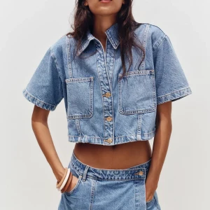 Croppad jeansskjorta från Zara - Säljer en croppad skjorta i ljusblå denim med korta ärmar och stora bröstfickor. Skjortan är från Zara i storlek M pga mindre i storlek! ALDRIG använd!!