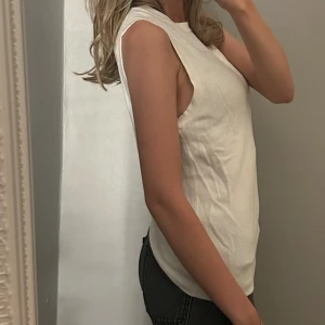 Vit ärmlös linnetopp - Säljer en stilren vit linnetopp med rund halsringning och rak passform. Toppen är ärmlös och har en enkel, clean look som passar perfekt till jeans eller kjol. Materialet känns mjukt och lätt mot huden, perfekt för varmare dagar.