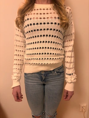 Vit stickad tröja med hålmönster - Snygg vit stickad tröja med lång ärm och coolt hålmönster över hela plagget. Tröjan har ribbade muddar vid ärmslut och nederkant, och en rundad halsringning. Tröjan är från Kappahl vet inte storlek men tror 170 eller S-M. Modellen är 158 cm..