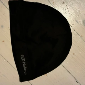 Svart träningsmössa från Kalenji - Svart mössa från Kalenji, perfekt för träning och löpning. Enkel och stilren design med diskret logga på kanten. Tillverkad i mjukt syntetmaterial som andas och sitter bekvämt på huvudet. Passar dig som vill ha en clean look när du är aktiv. Obs! Finns ej i Sverige.