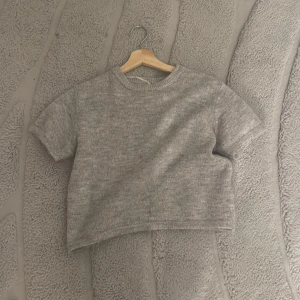 Grå stickad croppad tröja Gina Tricot - Grå stickad tröja från Gina Tricot i croppad modell med korta ärmar och rund hals. Perfekt för dig som gillar enkel och clean stil. Mjuk och skön känsla tack vare det stickade materialet. Passar till jeans eller kjol för en chill look.