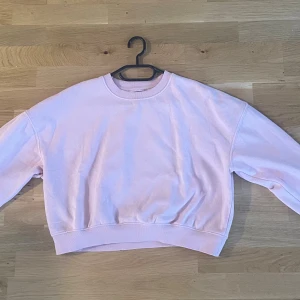 Ljusrosa sweatshirt från 157 XS/S - Ljusrosa sweatshirt från 157 i storlek XS. Tröjan har en klassisk rund hals, ribbade muddar och är tillverkad i mjuk bomullsmix med fleece på insidan. Passformen är loose och den är perfekt för chill dagar. Enkel och stilren design utan mönster eller tryck.