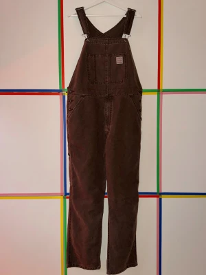 Bruna Levi's dungarees i jeans, stl L - Säljer ett par bruna Levi's dungarees i klassisk jeansmodell. Byxdressen har raka ben, stora fickor fram och bak samt justerbara axelband. Materialet är denim och färgen är mörkbrun. Supersköna, men tyvärr inte min stil — köptes till Halloween-outfit och användes således bara en gång!