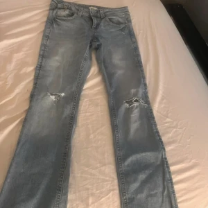 Ljusblå slitna jeans med raka ben - Ljusblå jeans med slitningar på knäna och snyggt tvättad finish. Raka ben och klassiska fickor både fram och bak med knappdetaljer. Jeansen har normal passform och är tillverkade i denim för en avslappnad look.