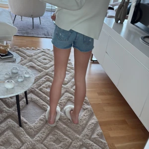 Blå jeansshorts med rå kant - Säljer ett par klassiska blå jeansshorts med rå, fransig kant och slitningar framtill. Modellen är kort och har fickor både fram och bak. Perfekta för varma dagar och en chill stil. Passar dig som gillar enkel denim och vill ha en tidlös look.