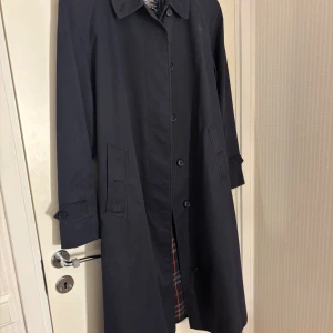 Burberry trenchcoat  - Klassisk trenchcoat i en mörkblå nyans. Jackan har en knäppning framtill, ett bälte i midjan och ett rutigt foder. Den har även fickor och detaljer vid ärmsluten.  Bältet har lite användningsslitningar och två små fläckar i fram men det försvinner säkert med rätt tvätt! Det står ingen storlek men skulle uppskatta den som någonstans mellan S-L beroende på önskad passform!   Pris kan diskuteras vid snabb affär!!