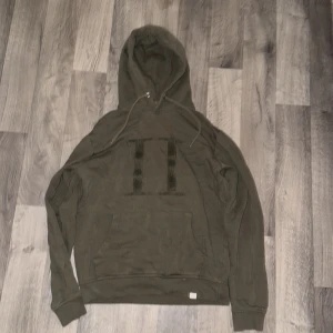 Olivgrön hoodie från Les Deux - Snygg olivgrön hoodie från Les Deux med stor broderad II-logga på bröstet. Tröjan har huva med snörning, magficka och långa ärmar. Tillverkad i mjuk bomull som är skön att bära. Perfekt för dig som gillar stilrena och coola detaljer. Passar S och M