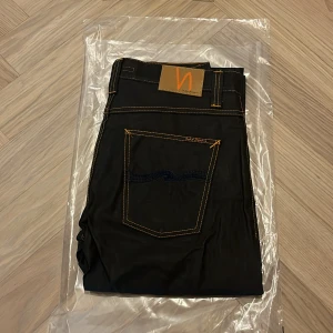 Helt nya nudie jeans co - grim Tim - W32 L34 - Helt nya och oanvända Nudie Jeans Co Grim Tim i den exklusiva färgen Dry Black Coated – fortfarande i originalförpackning (se bilder).  Detta är en av Nudies mest populära modeller, med en tidlös passform och den välkända premiumkvaliteten som gör Nudie till ett av Sveriges mest uppskattade jeansmärken.  Nypris: 1600  Detaljer: • Modell: Grim Tim • Storlek: W32 / L34 • Färg: Dry Black Coated (svart med lätt glans och vaxad look) • Passform: Regular slim fit – normal midja, rakare ben