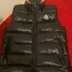 Svart dunväst från Moncler - Säljer en svart moncler väst den är riktigt snygg och bekväm. Västen har inga skador och är i ett bra skick fast den är använd ett fåtal par gånger. Den är 100% äkta, kvitto finns. Ny pris på jackan är 8000kr, kontakta om du vill veta mer!