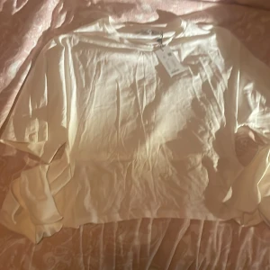 Vit omlottopp med knyt från lager157 - Säljer en vit omlottopp från 15 i storlek XL. Toppen har långa ärmar och ett brett knytband i midjan som ger en snygg omlotteffekt. Materialet är mjukt och lätt, perfekt för en stilren look. Enkel och clean design som passar till många outfits.