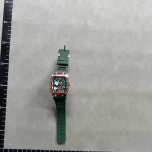 Richard Mille grön klocka med roséguld - Säljer en Richard Mille klocka med grön gummirem och en cool roséguldfärgad boett. Urtavlan har synliga mekaniska detaljer och en unik form som sticker ut. Perfekt för dig som gillar exklusiv design och vill ha något som verkligen syns på handleden.