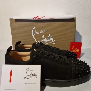 Svarta sneakers Christian Louboutin 43 - Säljer ett par svarta sneakers från Christian Louboutin med coola svarta nitar på tån. Skorna har snörning och är tillverkade i skinn och textil, med en platt sula och rund tå. Perfekta för dig som vill sticka ut med en edgy och lyxig stil.Låda ingår ej.