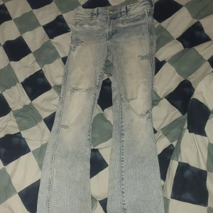 Bootcut ljusa jeans från H&M - Bootcut jeans från H&M i ljusblå tvätt med slitna detaljer och dubbla knappar i midjan. Låg midja och justerbar midja för perfekt passform. Klassisk femficksmodell i bomullsmix, perfekt för en avslappnad look.