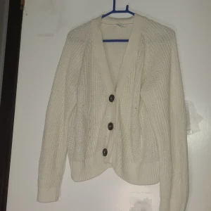 Vit stickad kofta från Lindex - Säljer en vit stickad kofta från Lindex med snygg ribbad kant och tre svarta knappar framtill. Koftan har långärmad passform och ett klassiskt mönster i stickningen. Perfekt för dig som gillar enkel och stilren look.