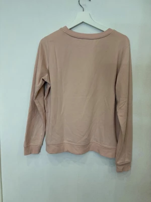Beige sweatshirt med tryck från KappAhl - Snygg beige sweatshirt från KappAhl med svart tryck framtill där det står 'Magnifique' och franska texter. Tröjan har rund hals, långa ärmar och ribbade muddar vid ärmslut och nederkant. Perfekt för dig som gillar coola prints och fransk vibe.