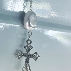 By prisförslag- 1 st Örhänge med pärla och korsberlock - Stilrent örhänge med en skimrande vit pärla och en detaljerad silverfärgad korsberlock. Hängsmycket har en klassisk krok och ger en cool och elegant vibe. Perfekt för dig som gillar unika accessoarer med lite edge.