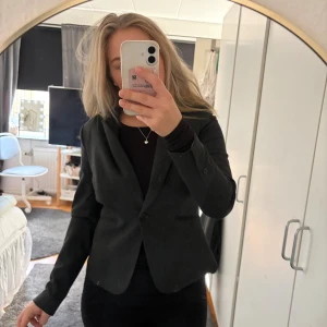 Grå kavaj från H&M - Klassisk från  kavaj från H&M med figurnära passform och enkel knäppning framtill. Kavajen har två fickor utan lock och är helfodrad med vit insida. Perfekt för en clean och stilren look. Använd fåtal gånger 