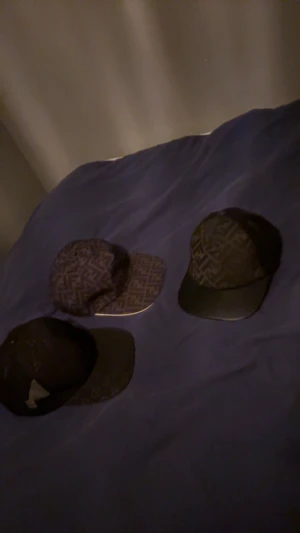 Fendi kepsar med monogrammönster - Tre snygga  kepsar med det klassiska FF-monogrammet i mörka färger. Två kepsar har tydligt rutigt Fendi-mönster och en har en diskret logga framtill. Alla har böjd skärm och justerbar passform, perfekta för att lyfta din streetstyle.