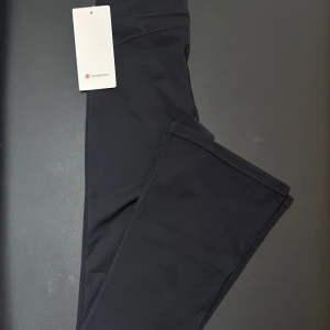 Flared Svarta leggings från Lululemon storlek 2 XS - Svarta flared leggings från Lululemon i storlek 2 XS, Tillverkade i ett stretchigt material av 77% nylon och 23% spandex. Hög midja och tight passform, perfekta för träning eller chill. Klassisk Lululemon-logga bak på linningen.