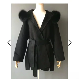 Svart kappa med pälsdetaljer och bälte - Snygg svart kappa med breda ärmar och fluffig päls på huvan. Jackan har omlottstängning och ett matchande bälte i midjan för extra stilpoäng. Perfekt för dig som vill ha en trendig och elegant look. Pris går att diskutera! 💗