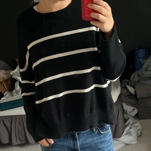 Svart randig stickad tröja - Svart stickad tröja med vita horisontella ränder. Modellen är loose fit med långärmade och rund hals. Perfekt för dig som gillar en chill och enkel stil. Passar till jeans eller andra casual outfits. Storlek XL från BikBok