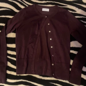 Mörklila kofta från Holly & Whyte - Snygg mörklila kofta från Holly & Whyte by Lindex i storlek XS. Koftan har rund hals, långa ärmar och silverfärgade knappar framtill. Materialet är mjukt och känns skönt mot huden, perfekt för lager-på-lager. Enkel och stilren design som funkar till många outfits.