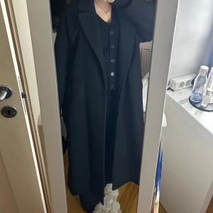 Svart lång kappa från Zara - - Nypris 1395kr. Säljer en svart lång kappa från Zara med klassisk krage, knytskärp i midjan och snygga knappar vid ärmsluten. 