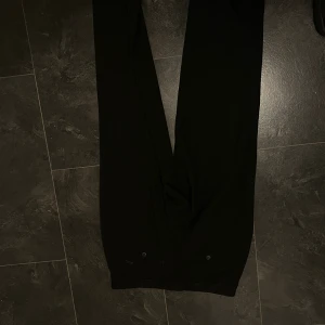 Svarta kostymbyxor med raka ben - Snygga svarta kostymbyxor med raka ben och klassisk passform. Byxorna har diskreta bakfickor med knappar och hällor för bälte. Perfekta för en stilren look och passar till många olika outfits.