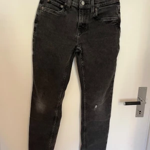 Levi's 502 svarta tapered jeans - Svarta Levi's 502 Regular Taper jeans med klassisk femficksdesign och snyggt avsmalnande ben. Jeansen har ett litet hål på ena benet och är tillverkade i mjukt denimtyg. Loggan på baksidan har börjat lossna lite. Barnstorlek!