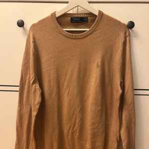 Beige stickad tröja Polo Ralph Lauren - Snygg beige stickad tröja från Polo Ralph Lauren i storlek M. Tröjan har rund halsringning och det klassiska broderade Polo-logot på bröstet. Perfekt för dig som gillar stilrena och tidlösa plagg med en soft vibe.
