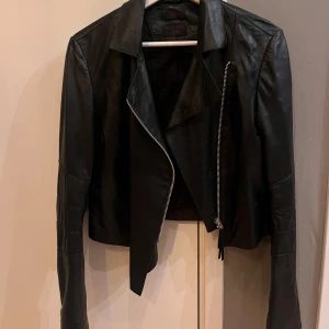 Svart skinnjacka från Tiger of Sweden - Snygg svart skinnjacka från Tiger of Sweden Jeans i klassisk bikerstil. Jackan har asymmetrisk dragkedja framtill, långa ärmar med dragkedjor vid ärmslut och coola sömdetaljer på armarna. Det är äkta tunnt skin. Nypris 6000 kr och den är knappt använd.