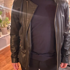 Svart skinnjacka Tiger of Sweden - Snygg svart skinnjacka från Tiger of Sweden Jeans i storlek Large. Jackan har raka linjer, silverfärgade dragkedjor fram och på fickorna samt en extra ficka på ärmen. Klassisk och stilren modell med lång ärm och normal passform. Fint tunnt svart skinn. Använd ett fåtal gånger. Nypris 6000kr