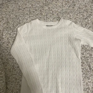 Vit kabelstickad tröja Basic You - Kabelstickad vit tröja från Basic You i ekologisk bomull. Tröjan har rund halsringning, lång ärm och klassiskt kabelmönster. Perfekt för lager-på-lager och passar till allt. Enkel och stilren design som funkar året runt.