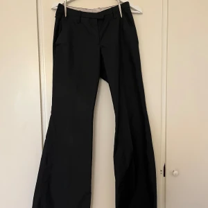 Svarta lågmidjade kostymbyxor med bootcut från J.Lindeberg - Svarta bootcut-kostym byxor från J.Lindeberg i 100% polyester. Lågmidjade. Byxorna har vida ben, klassiska fickor och hällor för bälte.