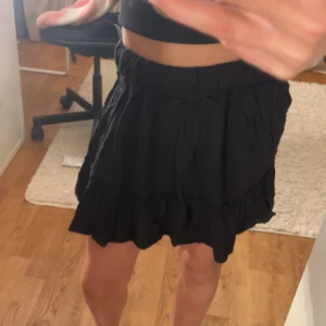 Svart volangkjol från SHEIN - Supersöt svart kortkjol från SHEIN med volangdetaljer och resår i midjan. Kjolen har en luftig och flowy känsla, perfekt att styla med crop tops eller stickade tröjor. Enkel att matcha och ger en chill vibe till outfiten.