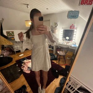 Vit kort klänning från Boohoo - Superfin vit kort klänning från Boohoo med broderade blommor och vida ärmar. Klänningen har fyrkantig ringning och är lätt utsvängd nertill. Perfekt för sommarens alla tillfällen och ger en fräsch och trendig look. Pas