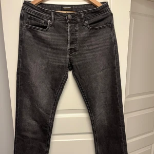 Svarta jeans från Jack & Jones, 30/32 - Säljer ett par svarta jeans från Jack & Jones i klassisk femficksmodell. Jeansen har en mörk tvätt, raka ben och normal passform. Tillverkade i bomull med en snygg, diskret slitning och detaljerade bakfickor. Nypris: 899kr. 