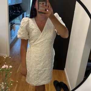 Vit omlottklänning från Kappahl - Supersöt vit omlottklänning från Kappahl med puffiga korta ärmar och strukturmönstrat tyg. Klänningen har knyt i sidan och v-ringning, vilket ger en riktigt fräsch och trendig look. Endast använd vid 1 tillfälle, perfekt att ha som studentklänning!
