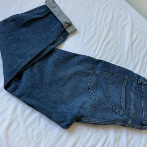 Blå jeans från Tiger of Sweden - Snygga blå jeans från Tiger of Sweden med klassisk femficksdesign och diskreta slitningar framtill. Jeansen har raka ben och normal passform, tillverkade i mjukt denimtyg med orangea sömmar och läderpatch bak i midjan.