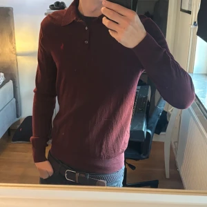 Ralph Lauren Rugbytröja - Säljer en vinröd långärmad pikétröja från Polo Ralph Lauren i mjuk merinoull. Klassisk krage, knäppning med två knappar och broderad logga på bröstet. Perfekt för dig som gillar stilrena och tidlösa plagg.
