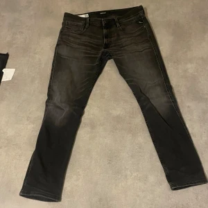 Svarta Replay jeans med slim fit - Snygga svarta jeans från Replay med diskret tvättad look och klassiska fem fickor. Jeansen har smal passform och raka ben, med Replay-logga på bakfickan och läderpatch i midjan. Perfekta för dig som gillar stilrena och moderna jeans.
