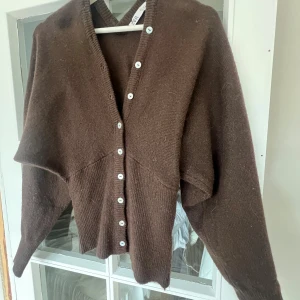 Figursydd kofta - Mysig brun stickad kofta från Zara med v-ringning och vita knappar hela vägen framtill. Koftan har lång ärm och en lite loose passform, perfekt att slänga på sig när det är kyligt. Ribbstickade detaljer nedtill och vid ärmslut.