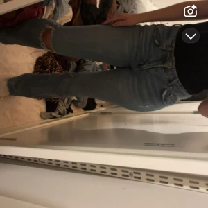 Blå bootcut jeans med slitningar - Säljer ett par blå bootcut jeans med slitningar på knäna. Jeansen har klassisk femficksdesign, normal passform och är tillverkade i jeansmaterial. Perfekta för en avslappnad och trendig look.