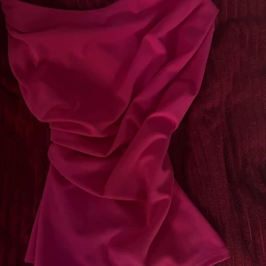 Ceriserosa topp från River Island - Säljer en ceriserosa topp från River Island med snygg drapering och en axel. Klänningen har en modern och trendig look, perfekt för dig som vill sticka ut. Materialet känns mjukt och följsamt mot kroppen.