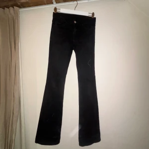 Svarta bootcut jeans med slitna benslut - Säljer ett par svarta jeans med bootcut passform och slitna benslut för en cool och avslappnad vibe. Jeansen har klassisk femficksdesign, knappstängning och är i ett stretchigt denimtyg som sitter snyggt över höften och låren. Säljer då jag inte riktigt får till att använda dom. Lite slitage i slutet av benen.