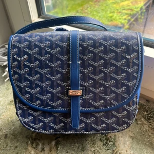 Blå axelväska  - Säljer en blå axelväska med deras ikoniska mönster i vitt och grått. Väskan har justerbar axelrem, silverfärgat spänne och detaljer i skinn. Kommer med original dustbag i gult. Perfekt för dig som vill sticka ut med en lyxig och unik accessoar.