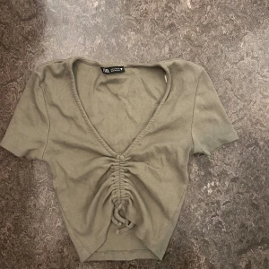 Grön ribbad croppad topp från Zara - Snygg ljusgrön croppad topp från Zara med korta ärmar och djup v-ringning. Toppen har ribbad struktur och cool snörningsdetalj, storlek S