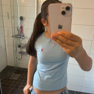 Ljusblå t-shirt från Polo Ralph Lauren - Säljer en ljusblå t-shirt från Polo Ralph Lauren med klassisk röd broderad logga på bröstet. T-shirten är i bomull, har rund halsringning och korta ärmar. Snygg och enkel modell som är lätt att matcha till jeans eller shorts.
